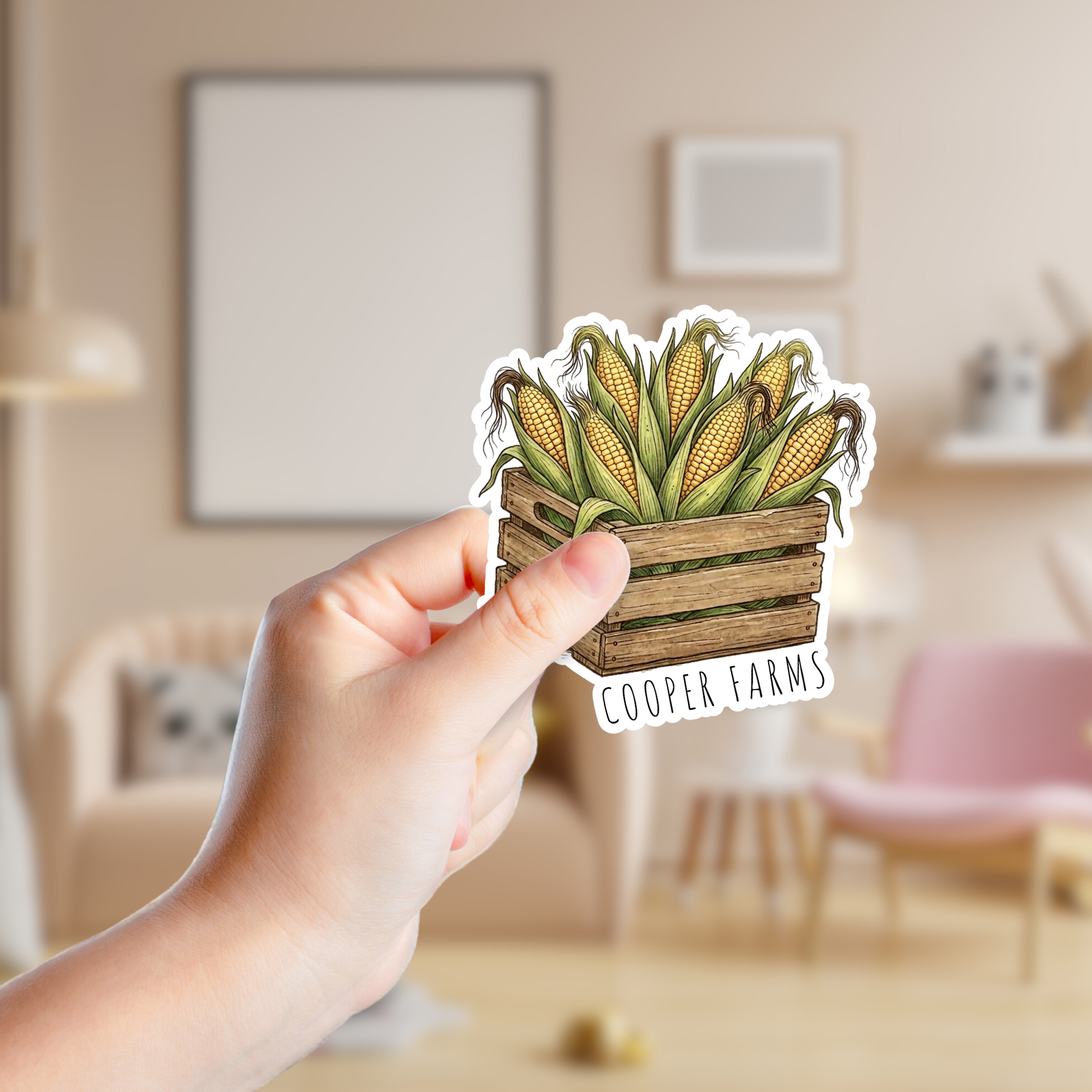 Hand holding a sticker of corn in a wooden crate with 'Cooper Farms' branding in a room.
