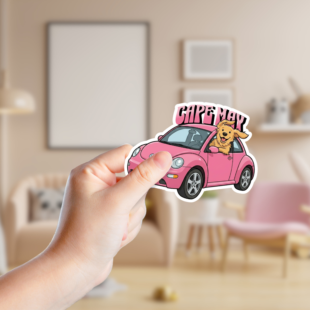 Hand holding a sticker of a pink car with a dog and 'Care Mal' text in a room.